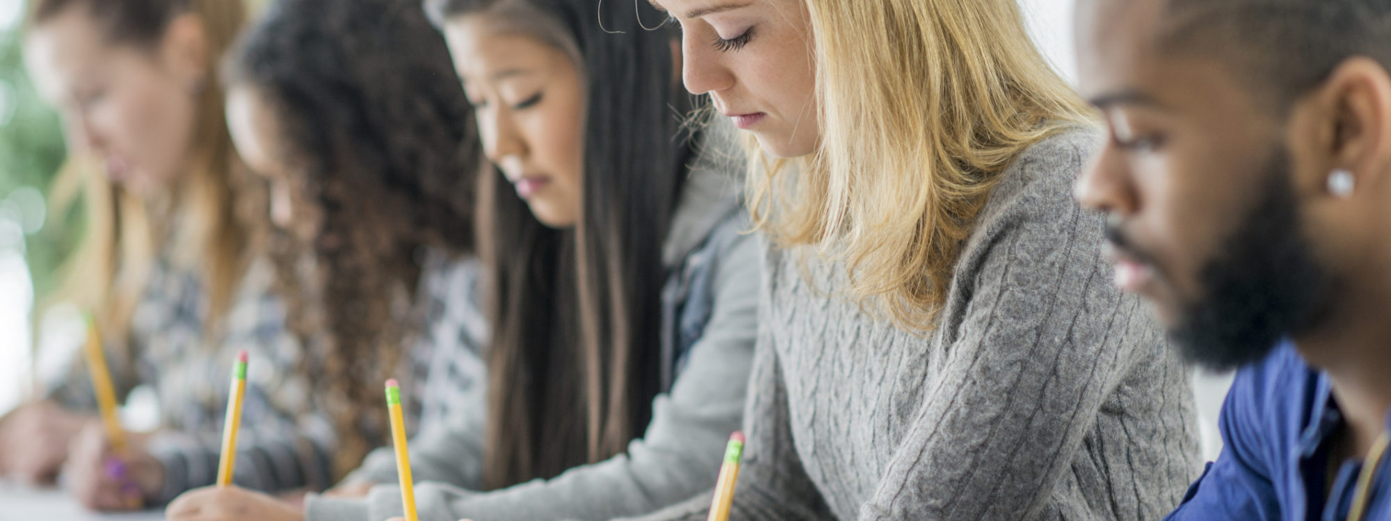 A multi-ethnic group of students are writing a university test. They are concentrating on the test.