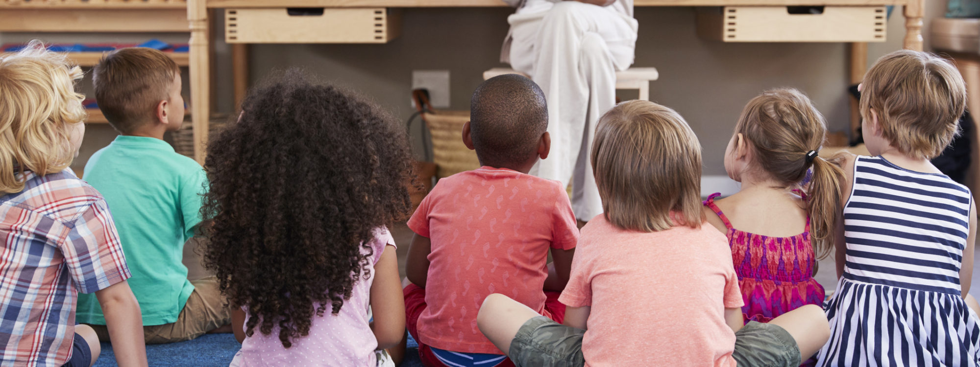 Teacher At Montessori School Reading To Children At Story Time