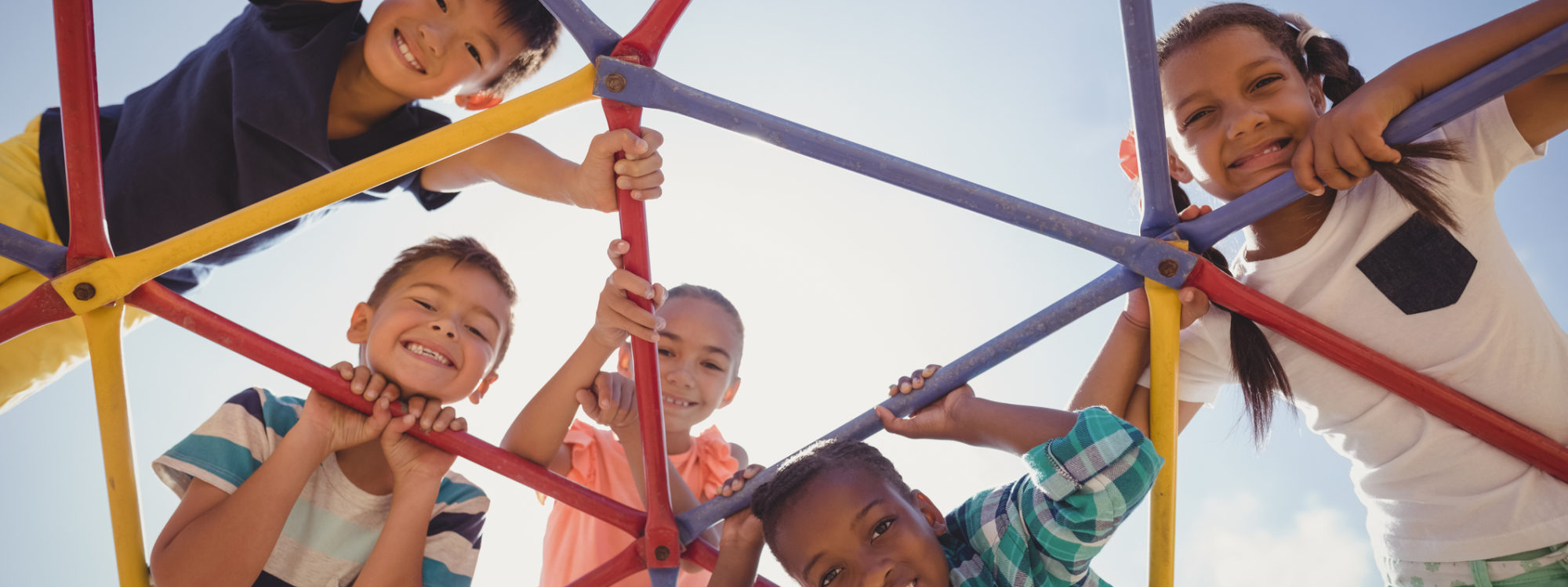 Portrait of happy schoolkids looking through dome climber at school playground