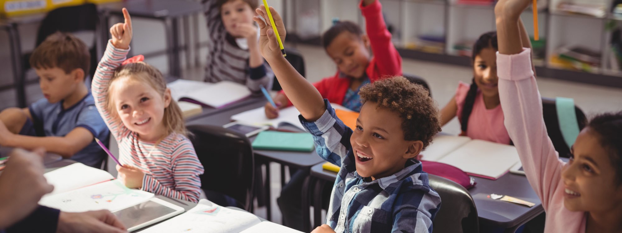 Schoolkids raising their hands in classroom at school