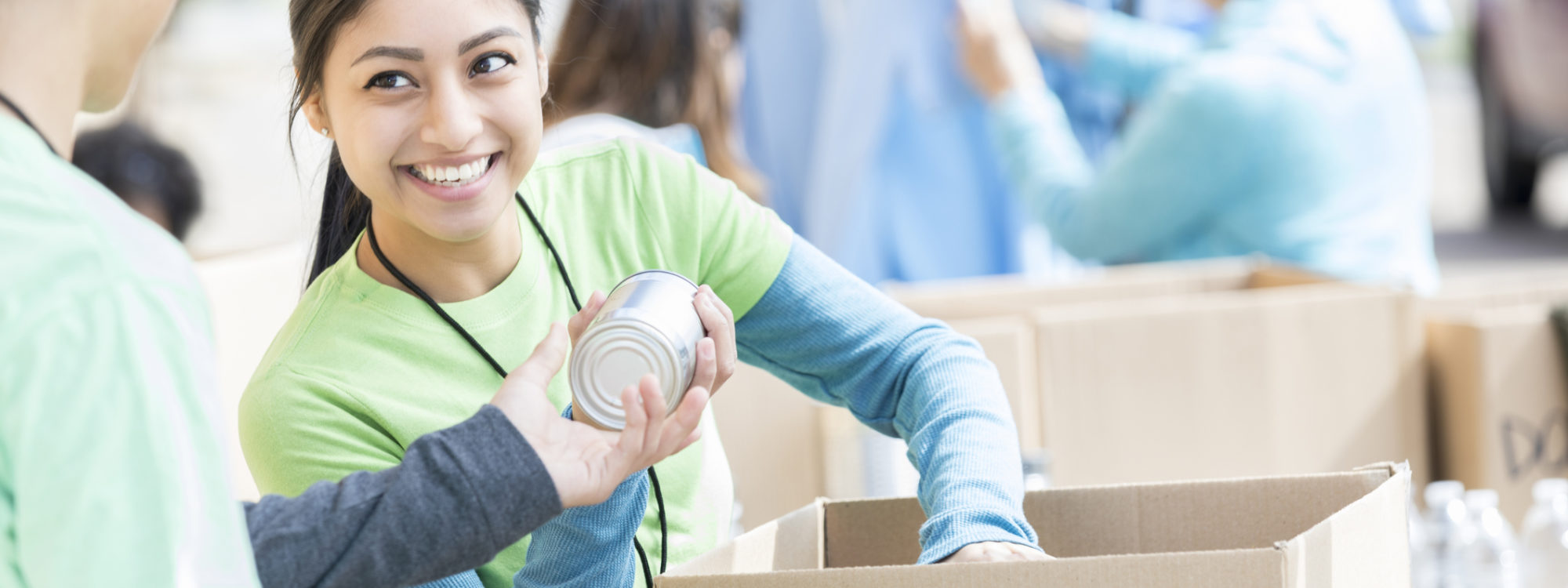 Male and female teenage food bank volunteers sort canned food items in cardboard boxes.
