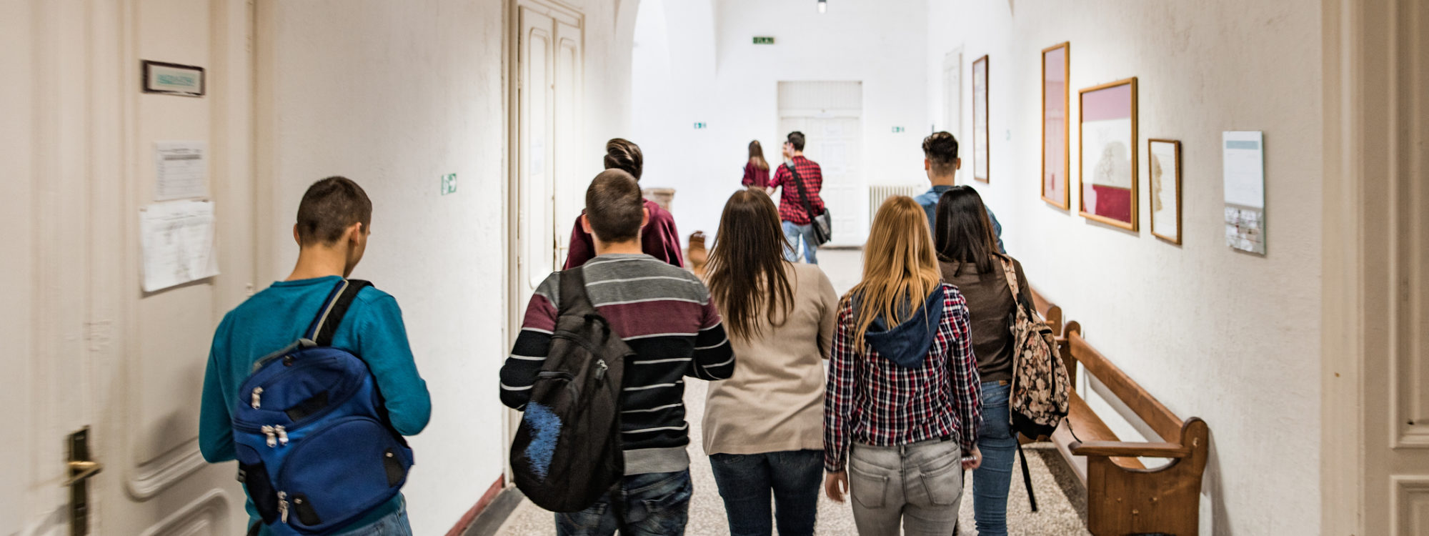 Rear view of high school students walking in the school hallway.