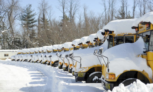 a line of parked busses covered in snow