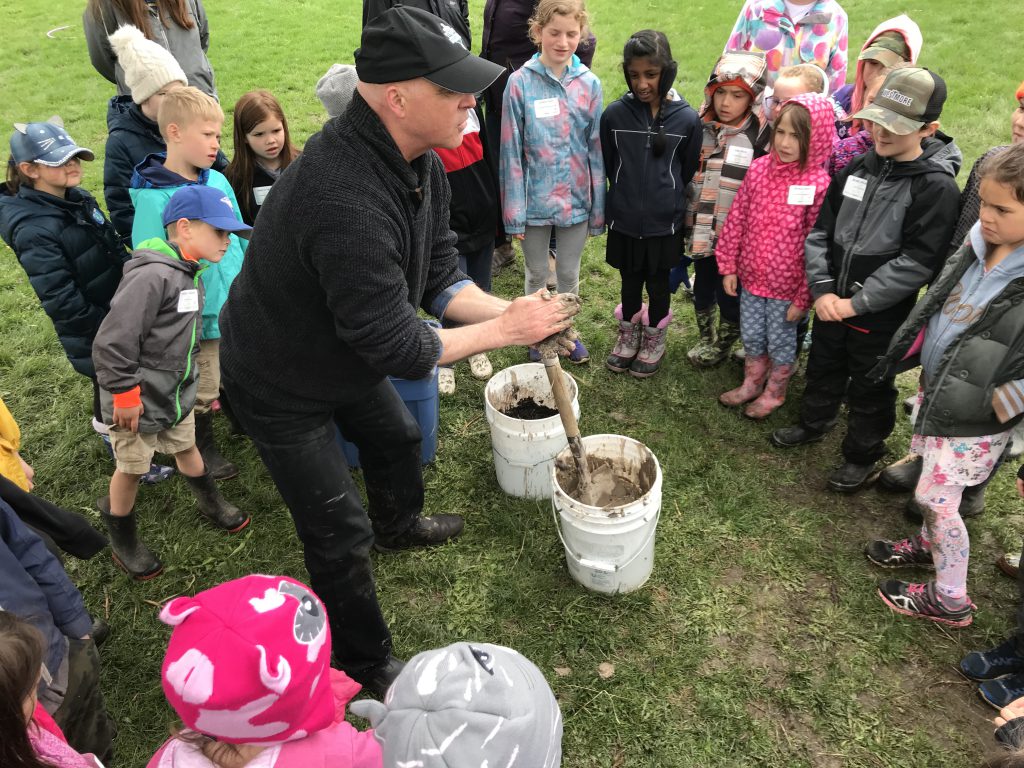 man holding mud in hands surrounded by students
