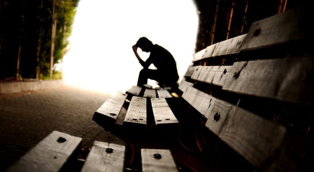 man holding head in hand on bench