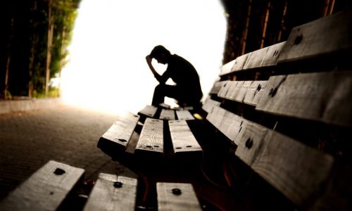 man holding head in hand on bench