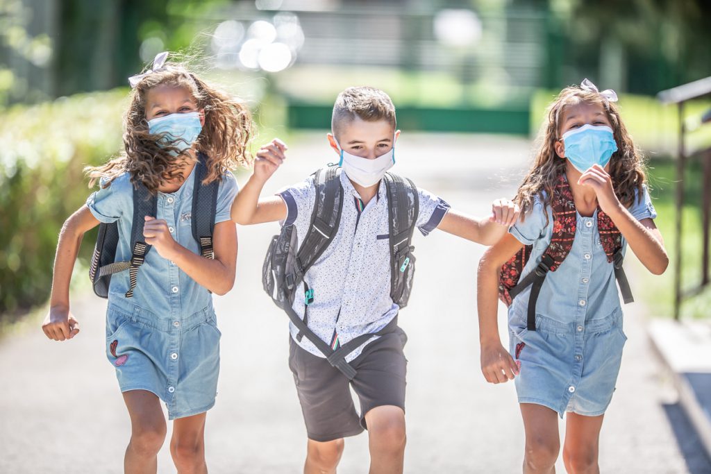 Happy schoolchildren with face masks run from the joy of returning to school