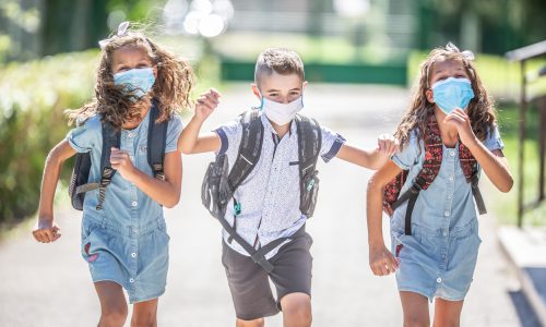 Happy schoolchildren with face masks run from the joy of returning to school