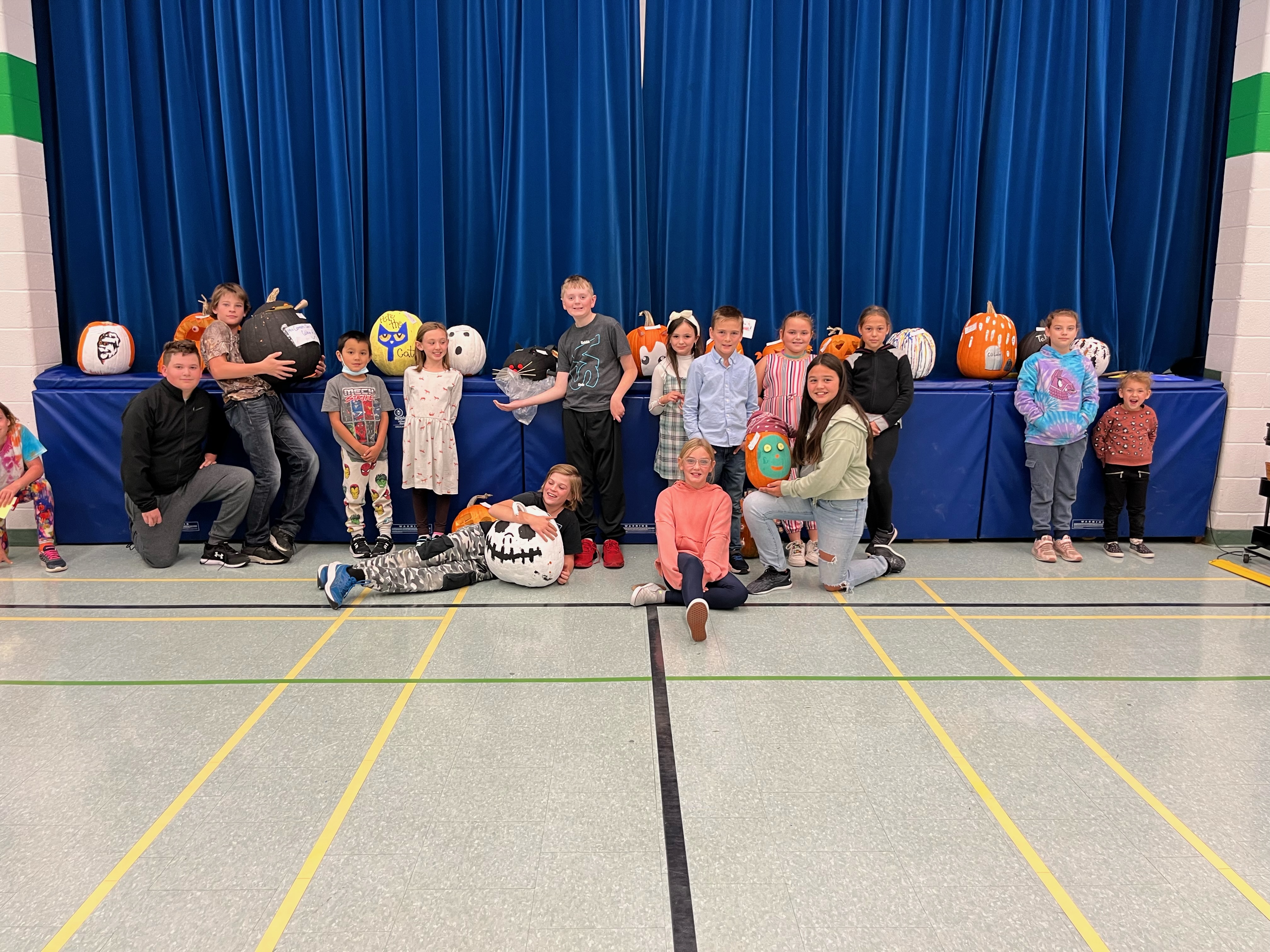 Students lined up in a gym displaying colourful pumpkins