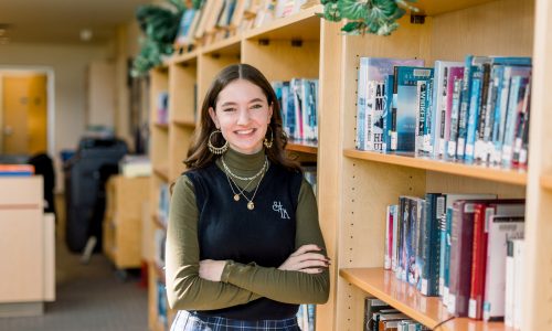 Female student leaning against a book shelf