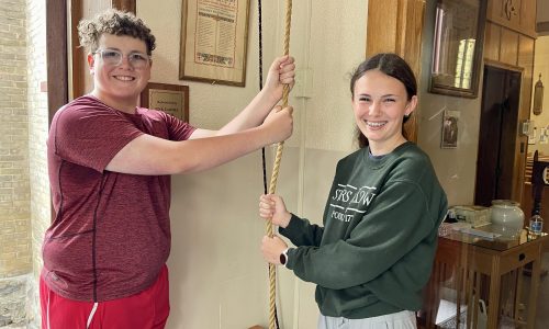 Students hold a bell rope in a church