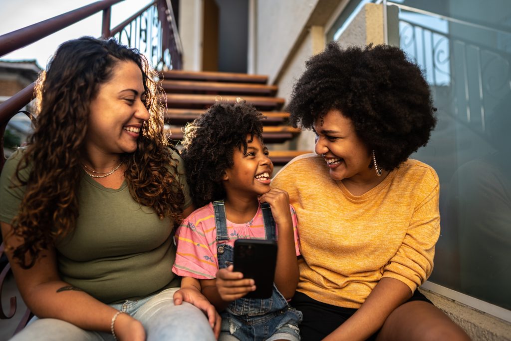 Image of a child with a smart phone enjoying a laugh with two adults