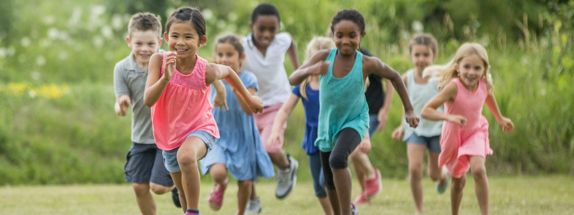 A multi-ethnic group of elementary age children are playing together outside at recess. They are chasing each other and are playing tag.