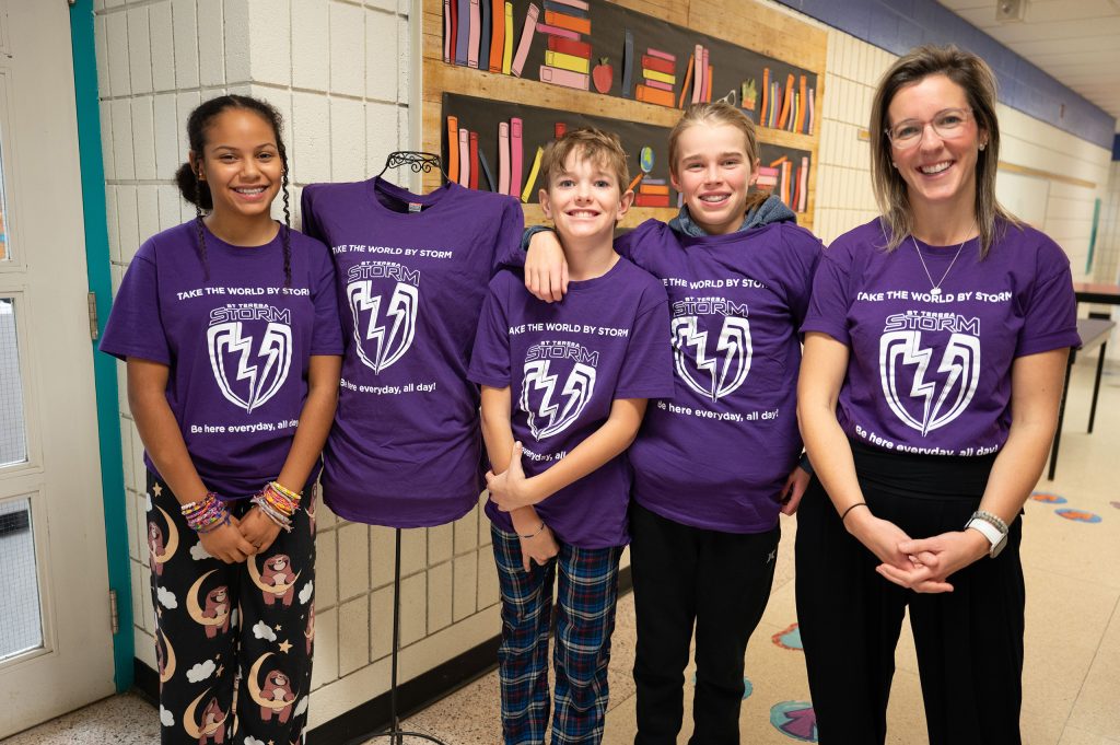 Three students stand with their teacher in front of the library.