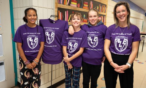 Three students stand with their teacher in front of the library.