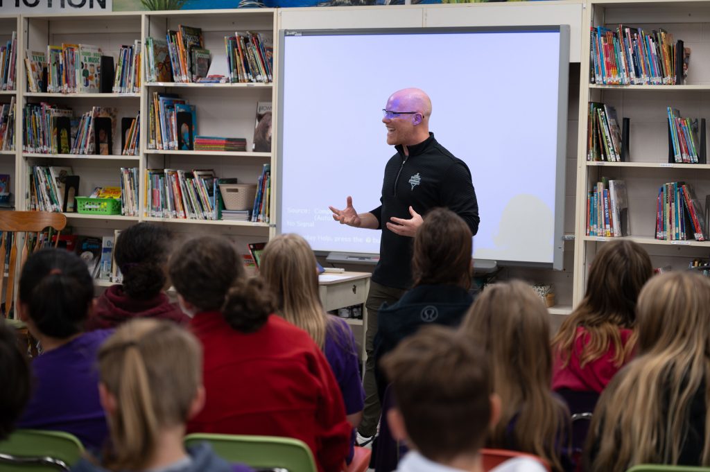 Classroom full of students listening to a presenter at the front of the room.