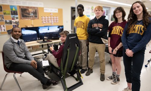 Students and an instructor gather around a flight simulator at a secondary school.