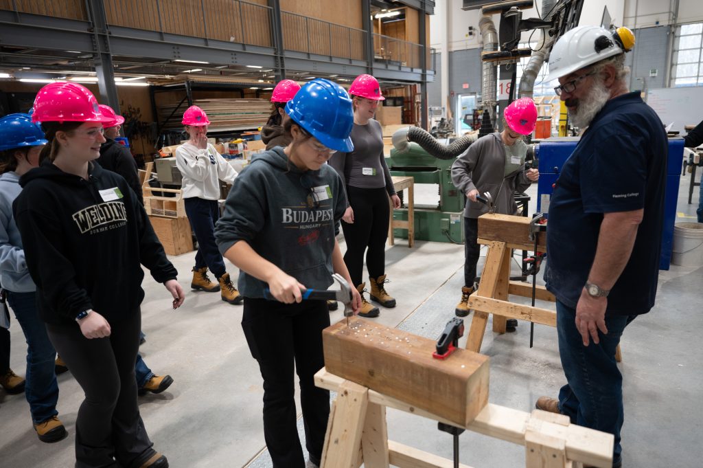 Group of girls in hard hats swinging hammers in a carpentry class.