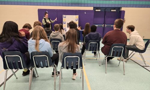 Group of students sitting in chairs while listening to a presenter.