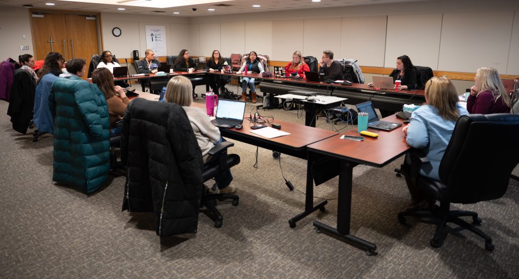 Group of educators and community members sitting around a large rectangular table section.