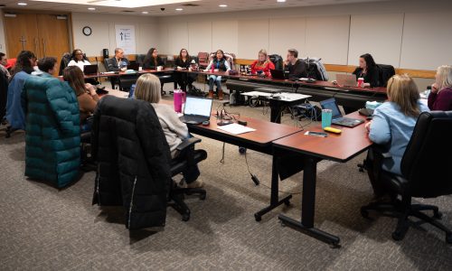 Group of educators and community members sitting around a large rectangular table section.