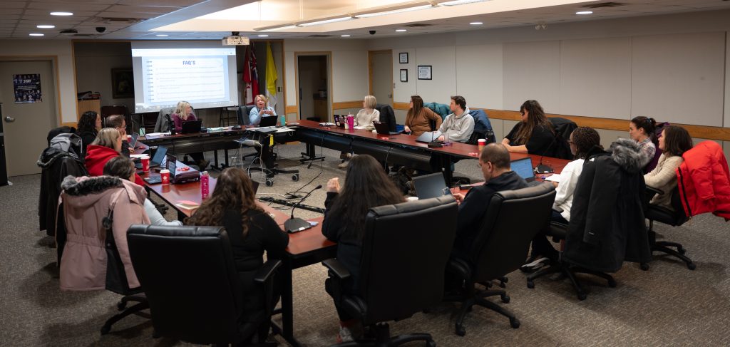 Group of educators and community members sitting around a large rectangular table section.