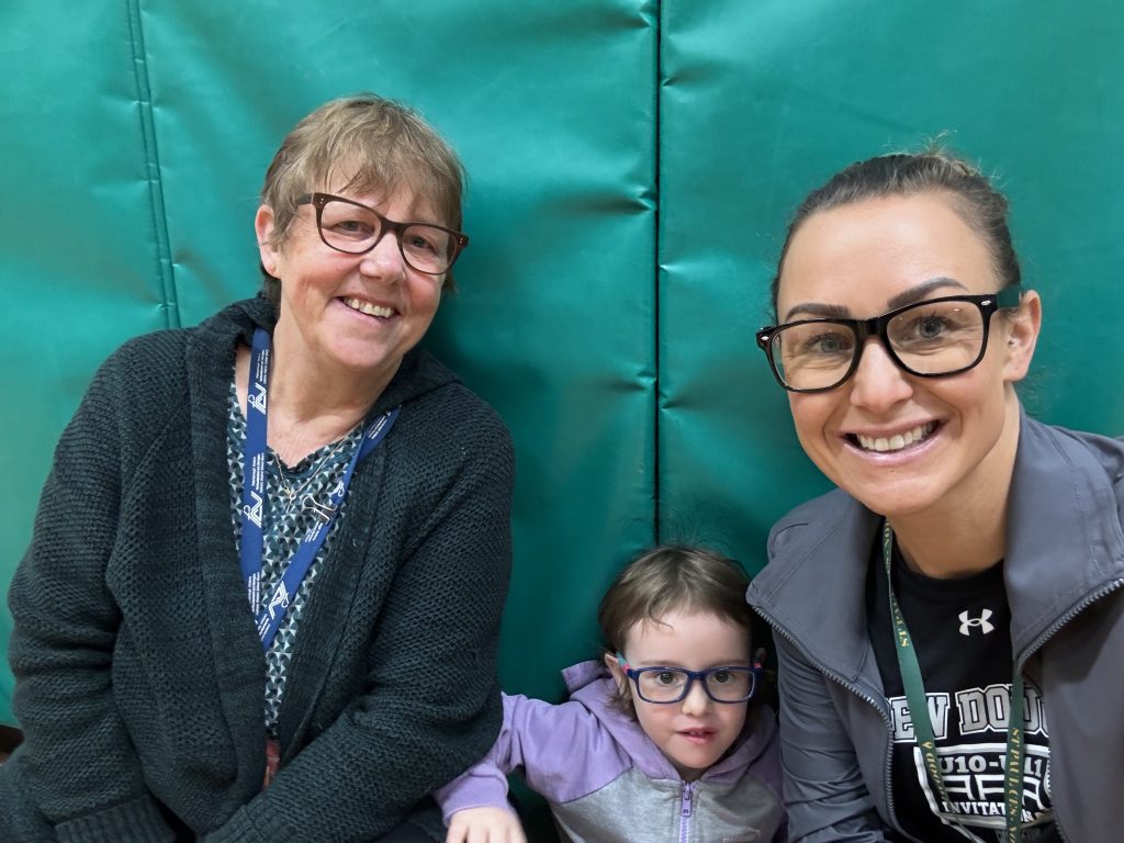 Two educators wearing glasses sit with student who's wearing glasses.