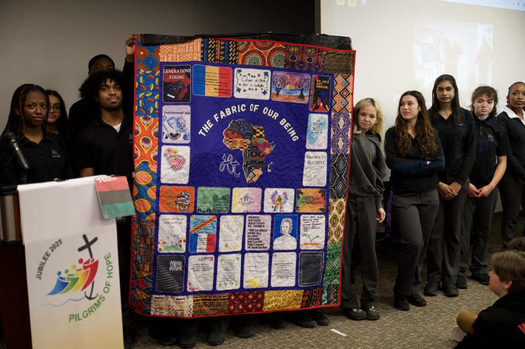 Group of students hold up a quilt created for Black History Month.