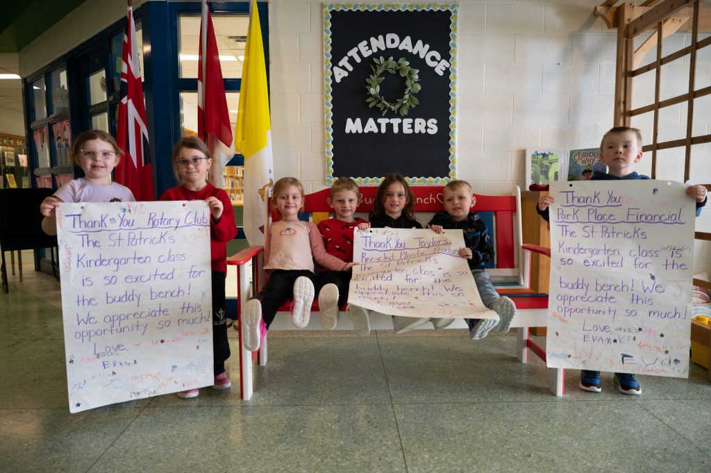 Group of students posing on a bench at a school.