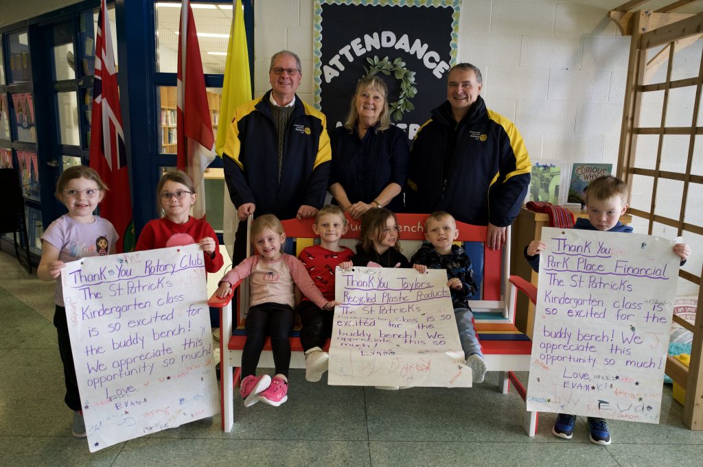 Group of adults and children pose around a bench at a school.