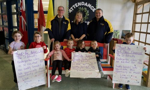 Group of adults and children pose around a bench at a school.