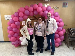 Three adults standing in front of pink display for Pink Shirt Day
