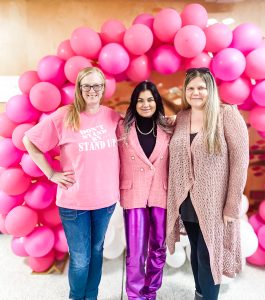 Three women standing in front of a pink display with balloons for Pink Shirt Day
