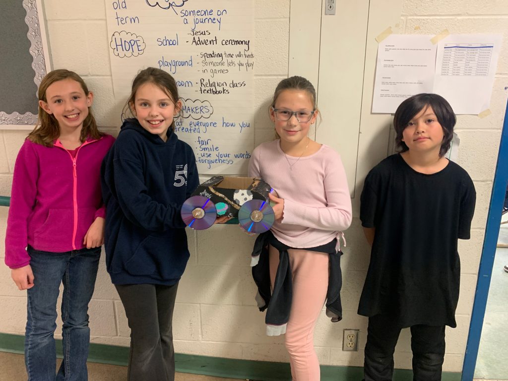 Four students pose with a small car created from items from a junk drawer.