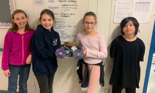 Four students pose with a small car created from items from a junk drawer.