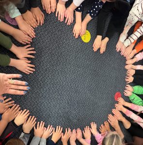 Group of students with their hands on the floor in a circle.