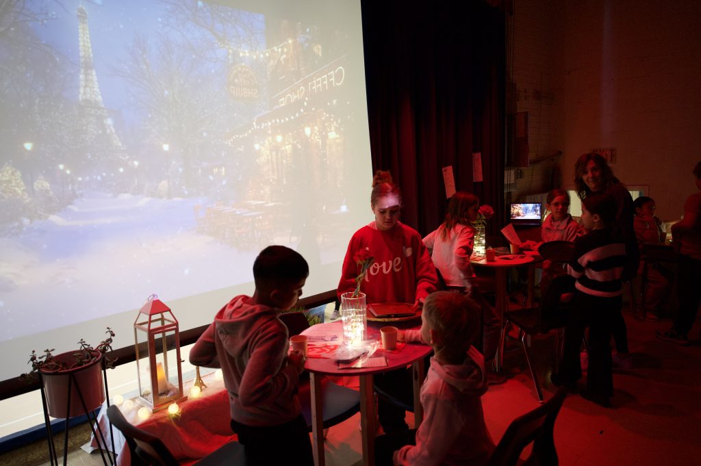 Group of students host a french cafe on the stage of a school gym.