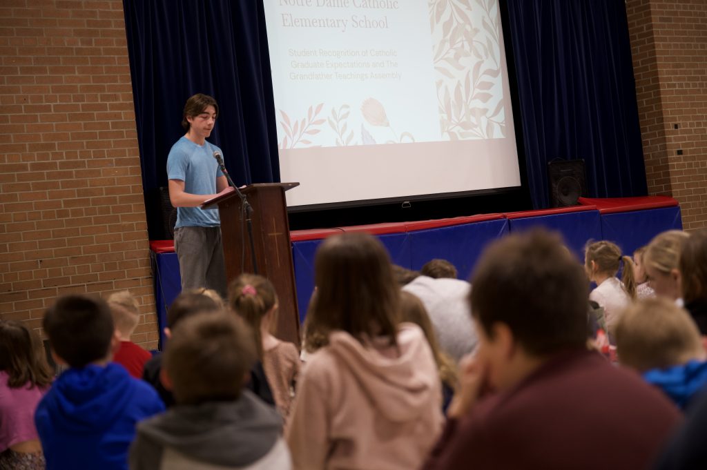 Student presents at lectern while group of younger students looks on.