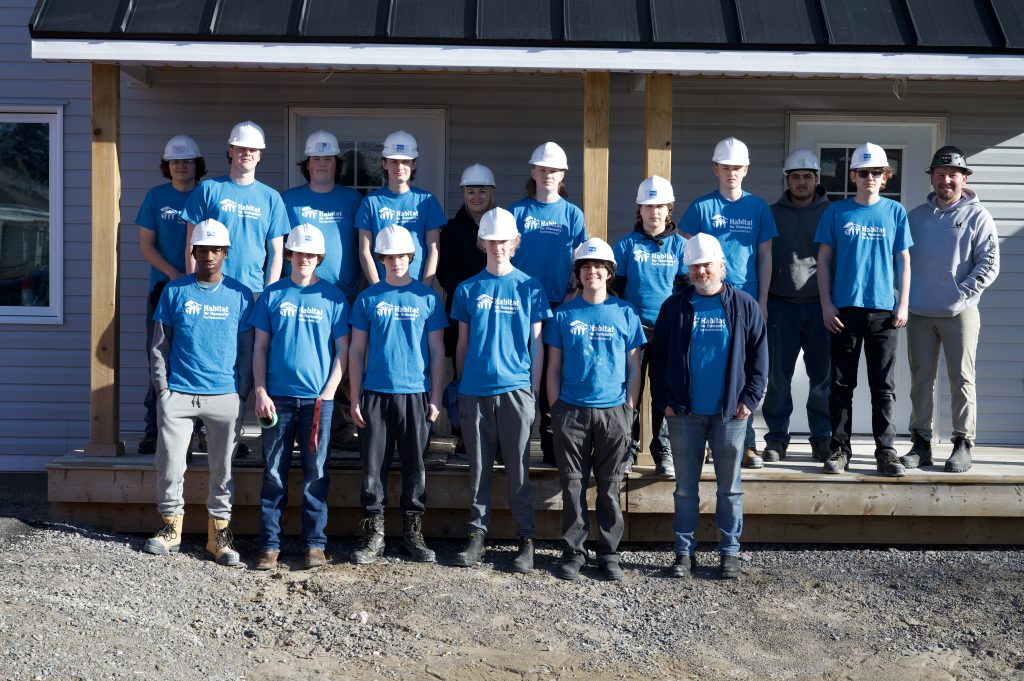 Group of students and adults in hard hats standing in front of a townhouse build for Habitat for Humanity.