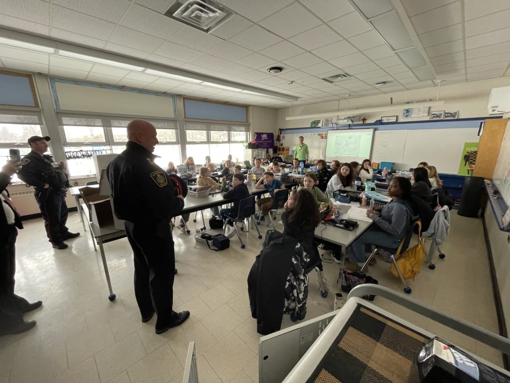 Police officers speak to a class full of students.