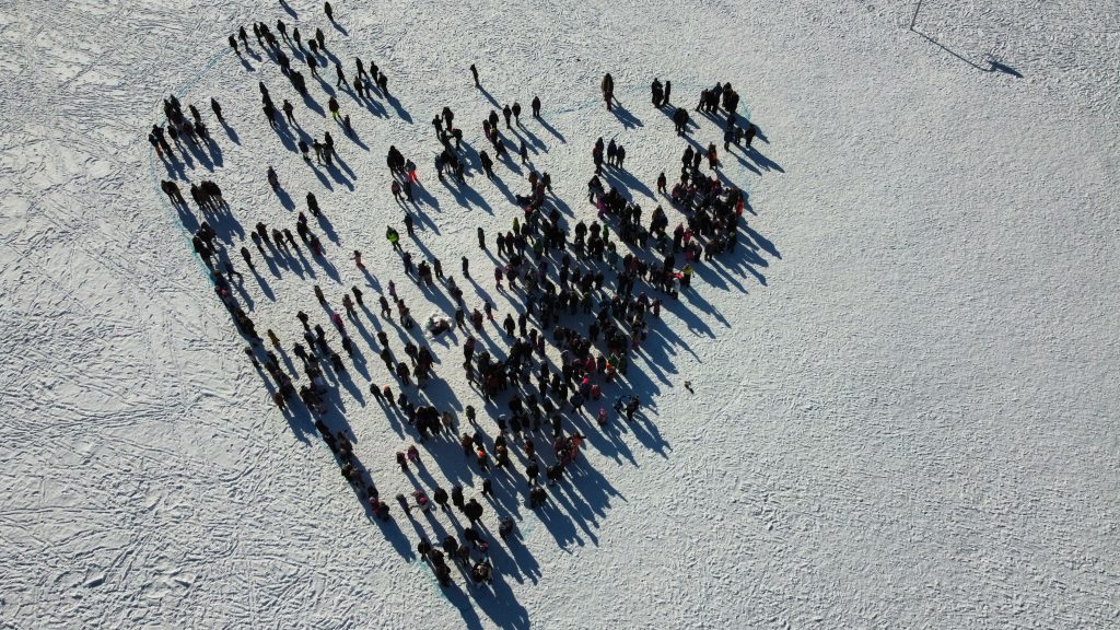 Group of students and staff gathered in a heart shape on the ground while a drone takes their photo from above.
