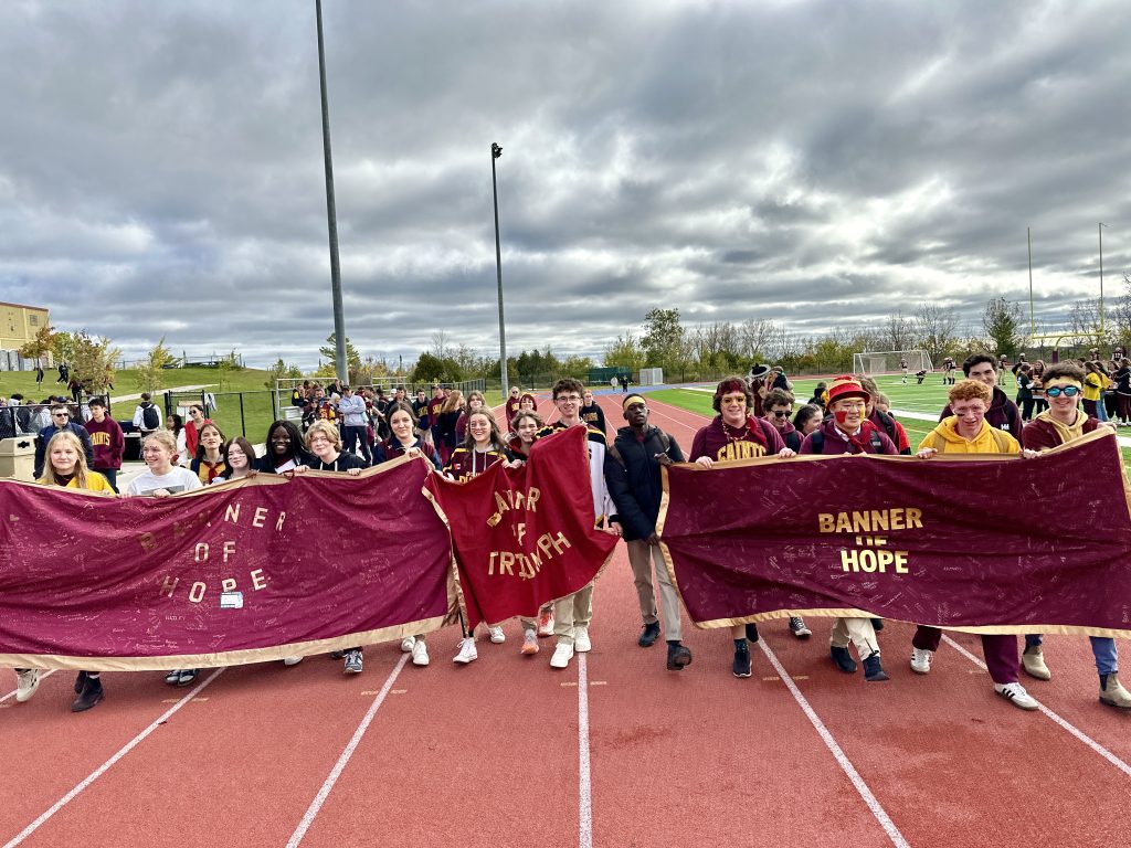 Students hold banners as they walk around a track at a school.