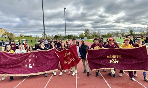 Students hold banners as they walk around a track at a school.