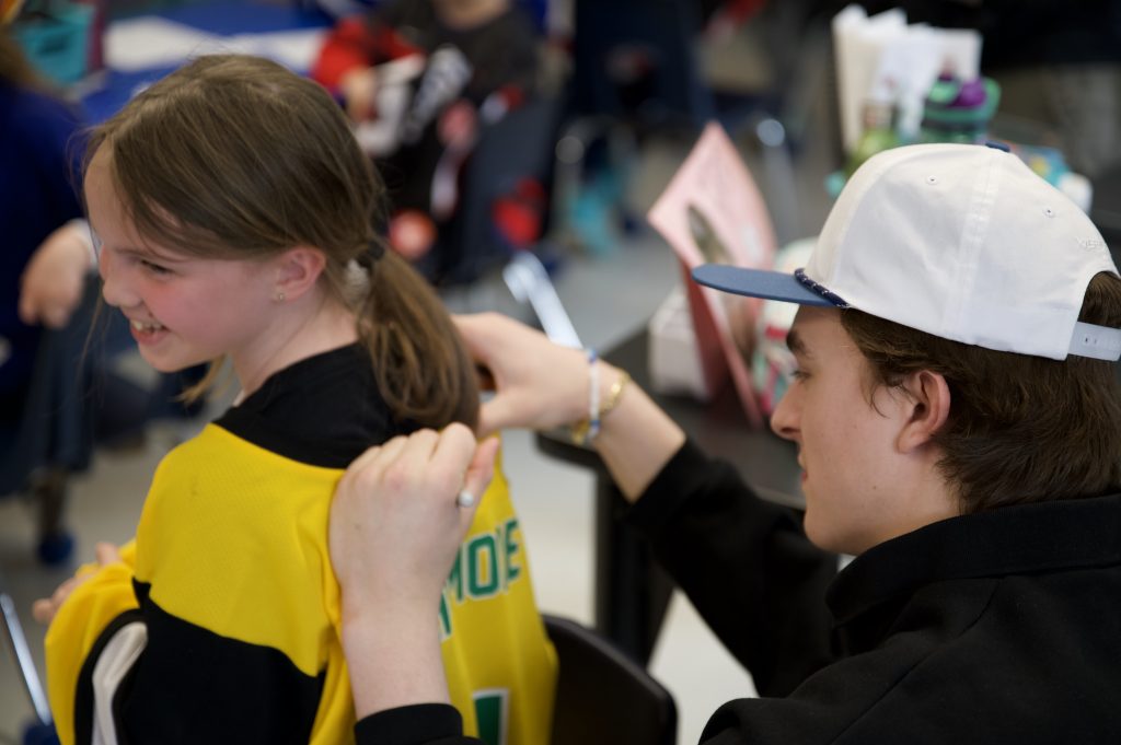 A hockey player signs the back of a child's jersey.