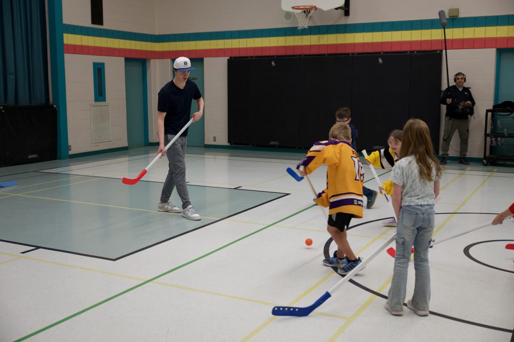 A game of floor hockey in a school gymnasium.