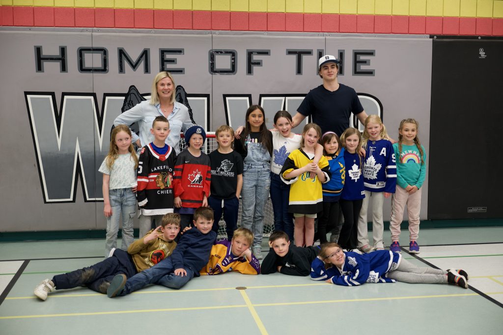 A group of students and a teacher poses with a hockey player in a gymnasium.