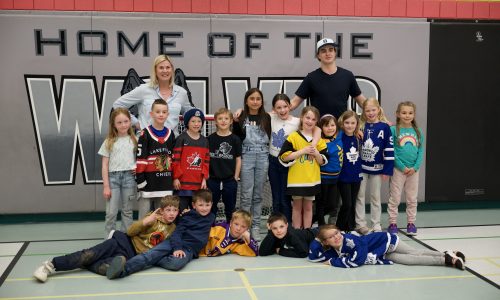 A group of students and a teacher poses with a hockey player in a gymnasium.