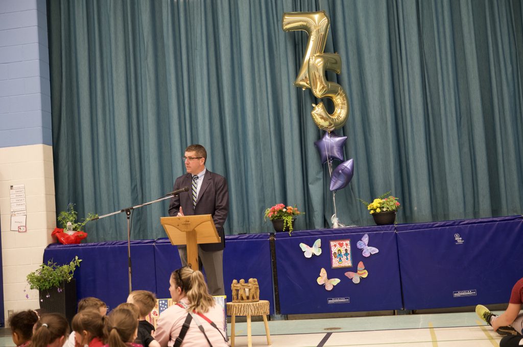 Adult gives a speech at a school assembly in a gym.