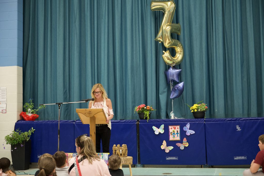 Adult gives a speech at an assembly in a school gym.