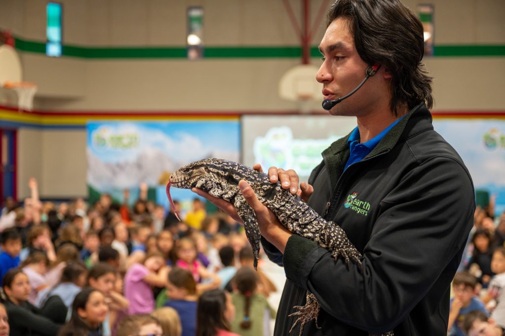 Man holds a lizard at a school assembly